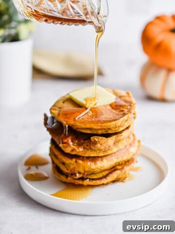 Maple syrup is being poured onto a stack of pumpkin pancakes.