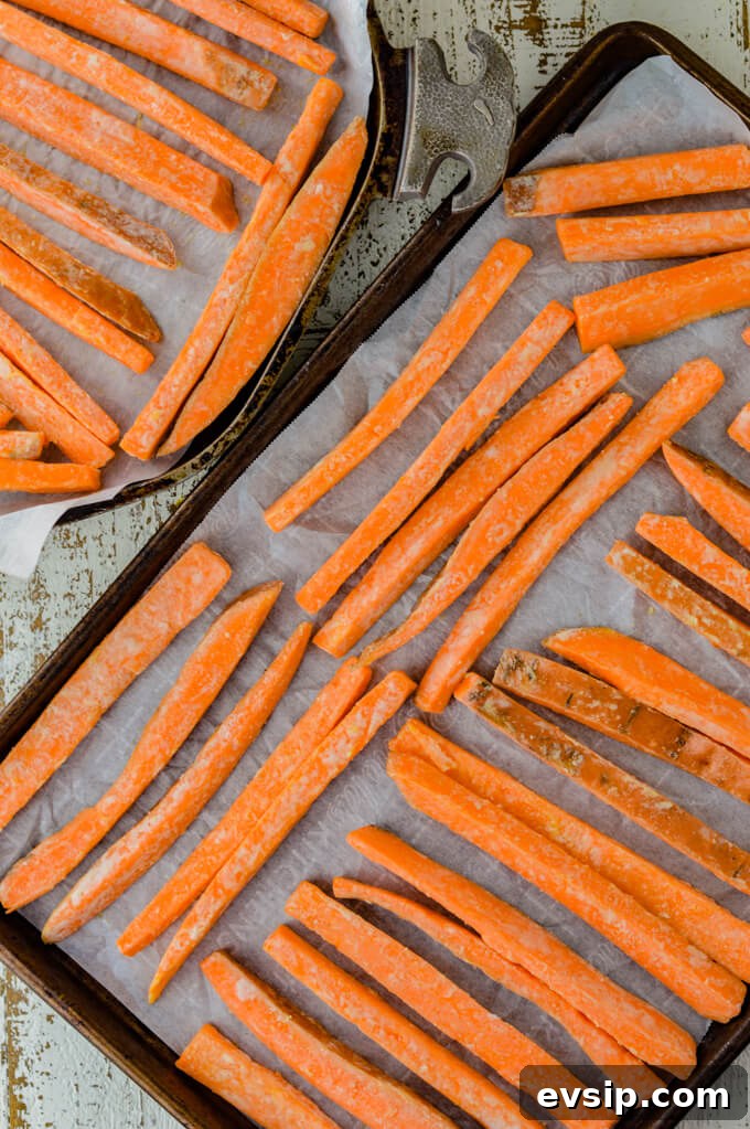 A rectangular cooking sheet and a circular pan, both with parchment paper on them and rows of raw sweet potato fries.