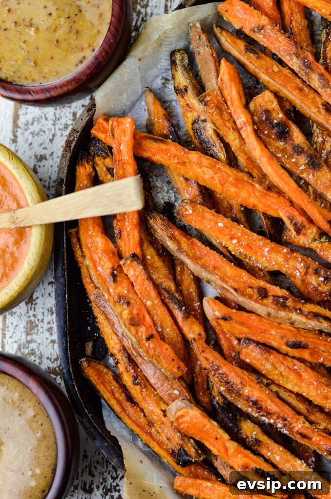 A baking sheet with parchment paper and baked sweet potato fries sit on it. Three dipping sauces sit next to the pan. 