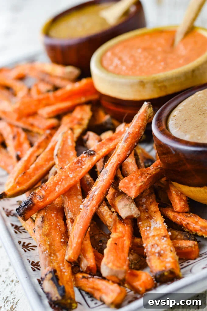 A platter of baked sweet potato fries with 3 bowls of dipping sauce sits next to them. 