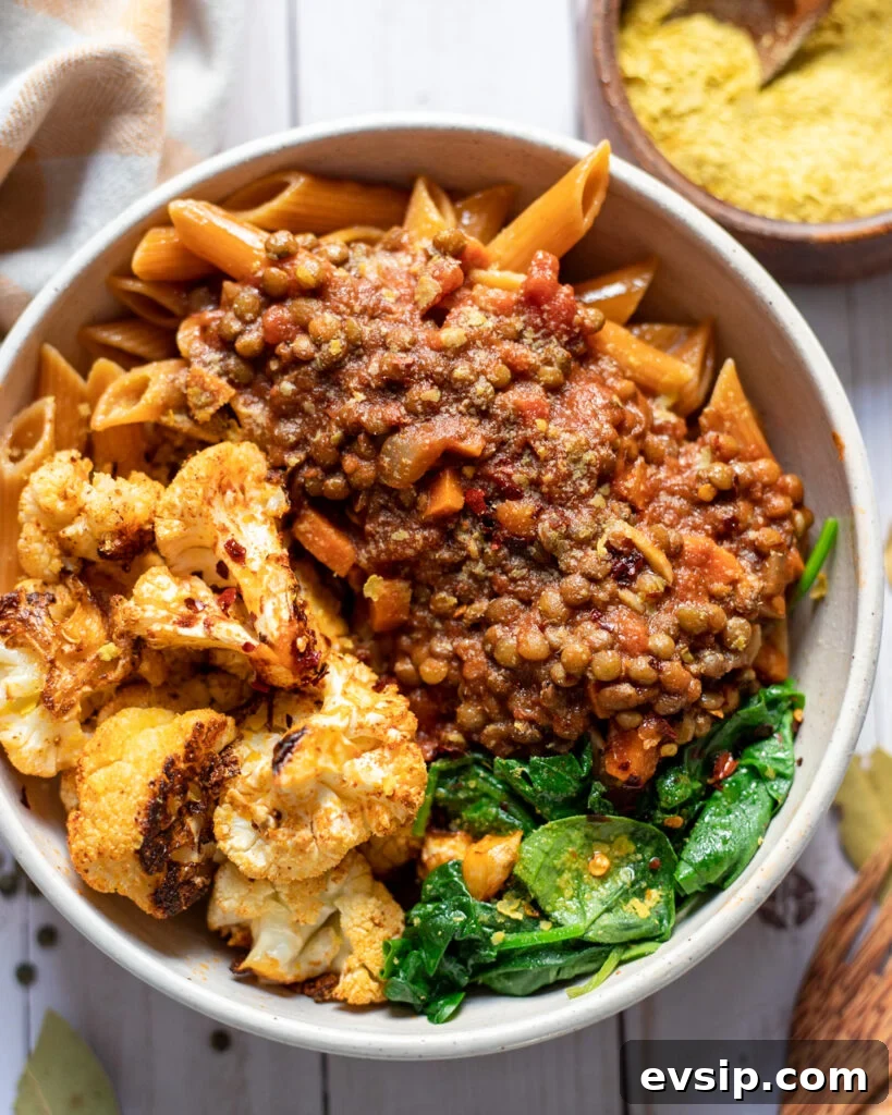 French Green Lentil Bolognese Recipe for Hearty Weeknight Meals 2 overhead view of a white serving bowl with homemade vegan lentil bolognese with green lentils, carrot, tomatoes, and more served with spinach and cauliflower over pasta.