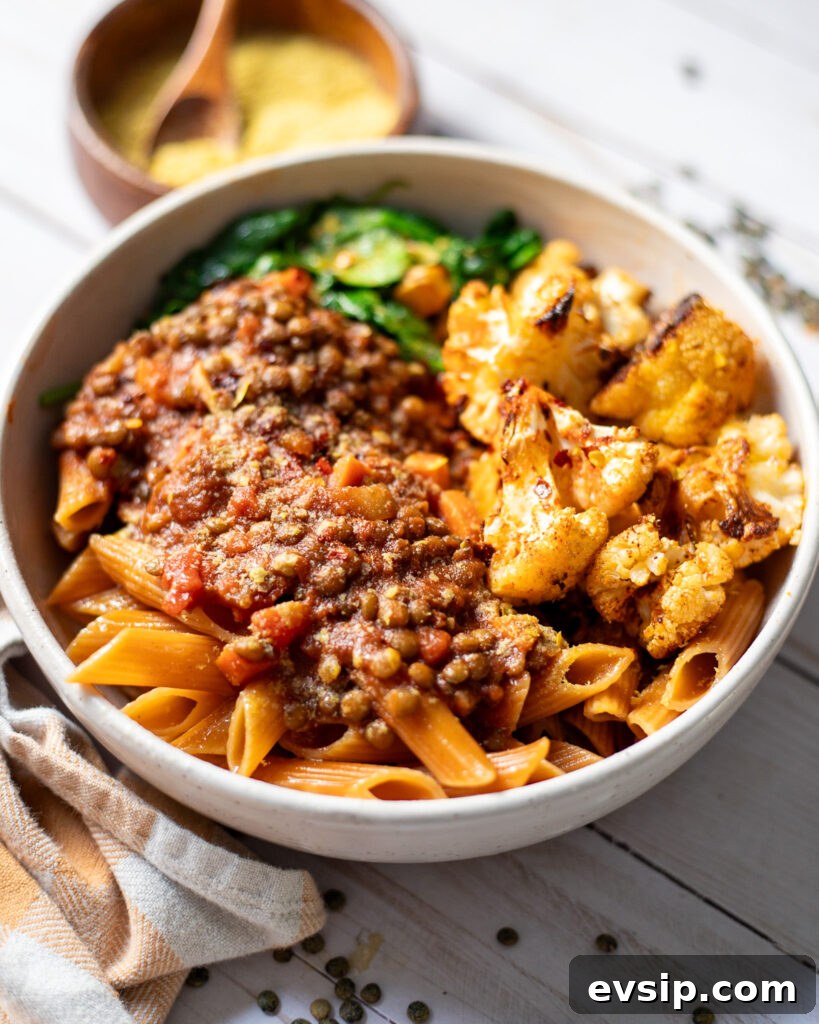 French Green Lentil Bolognese Recipe for Hearty Weeknight Meals 5 side view of a bowl with vegan bolognese made with green French lentils served with chickpea pasta, roasted cauliflower, and wilted spinach.