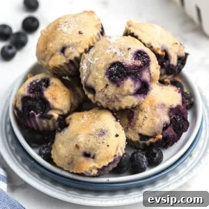 Blueberry muffins stacked on a white plate with fresh blueberries scattered around the table.