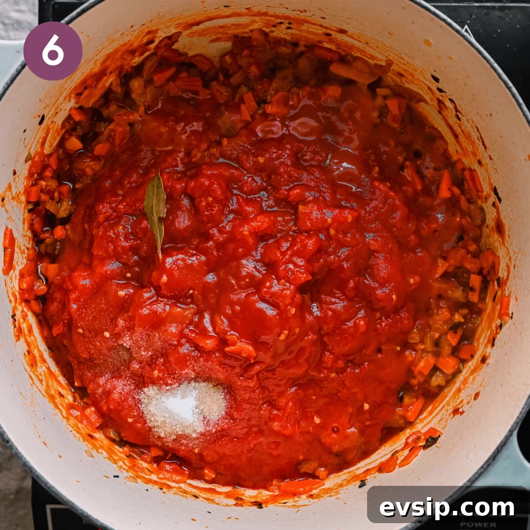 crushed tomatoes poured into a dutch oven with salt and herbs on top of sauteed onions and carrots. 
