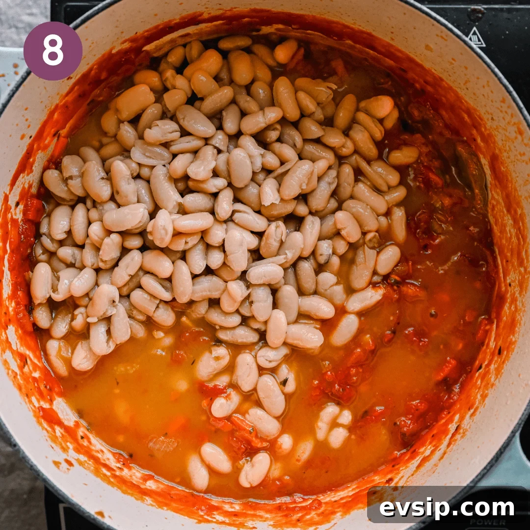 cannellini beans sitting on top of an italian tomato stew with vegetable broth in a dutch oven. 