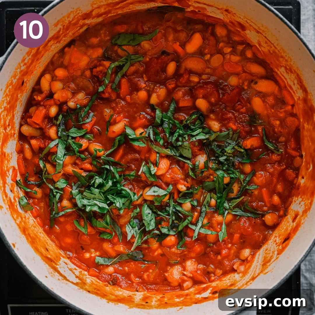 slivered basil garnished on top of thick and rich tuscan stewed beans with tomatoes in a dutch oven.