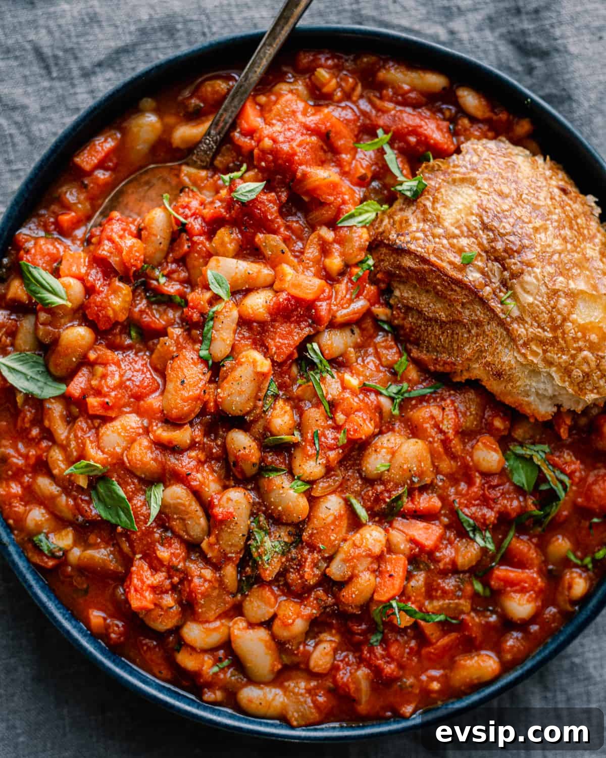 livornese stewed beans in a bowl bowl with a piece of bread on blue tablecloth