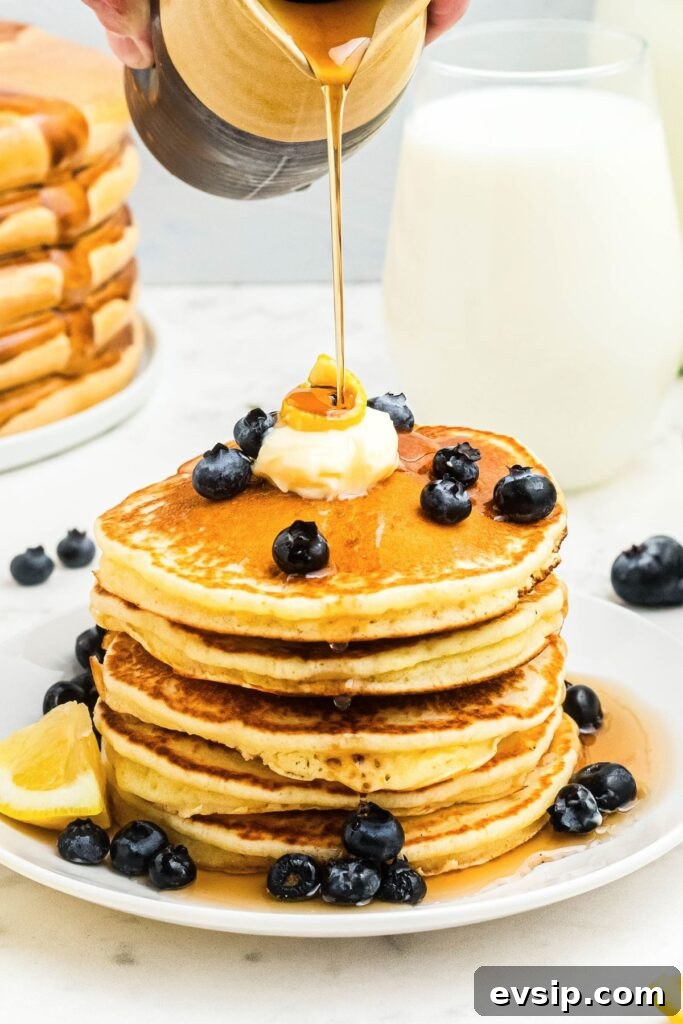 Fluffy Lemon Pancakes with Zesty Syrup Recipe 2 Golden fluffy lemon pancakes stacked on a white plate with syrup being poured on top.