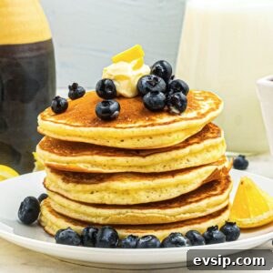 Fluffy Lemon Pancakes with Zesty Syrup Recipe 8 Golden fluffy pancakes stacked on a white plate, topped with blueberries and butter.