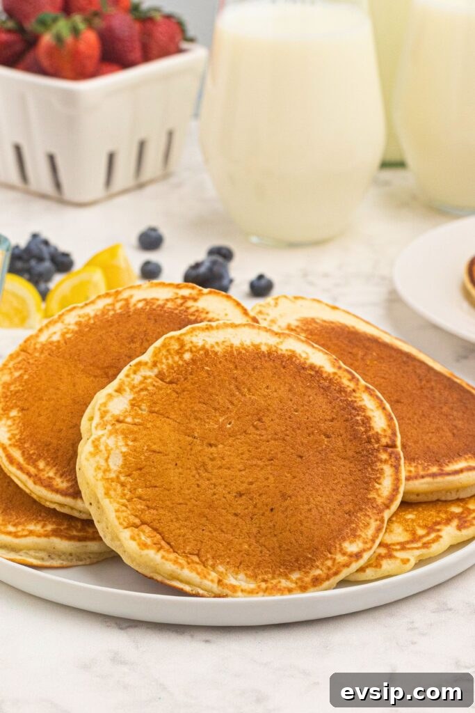 Fluffy Lemon Pancakes with Zesty Syrup Recipe 6 Stacked golden brown and fluffy pancakes on a white plate.