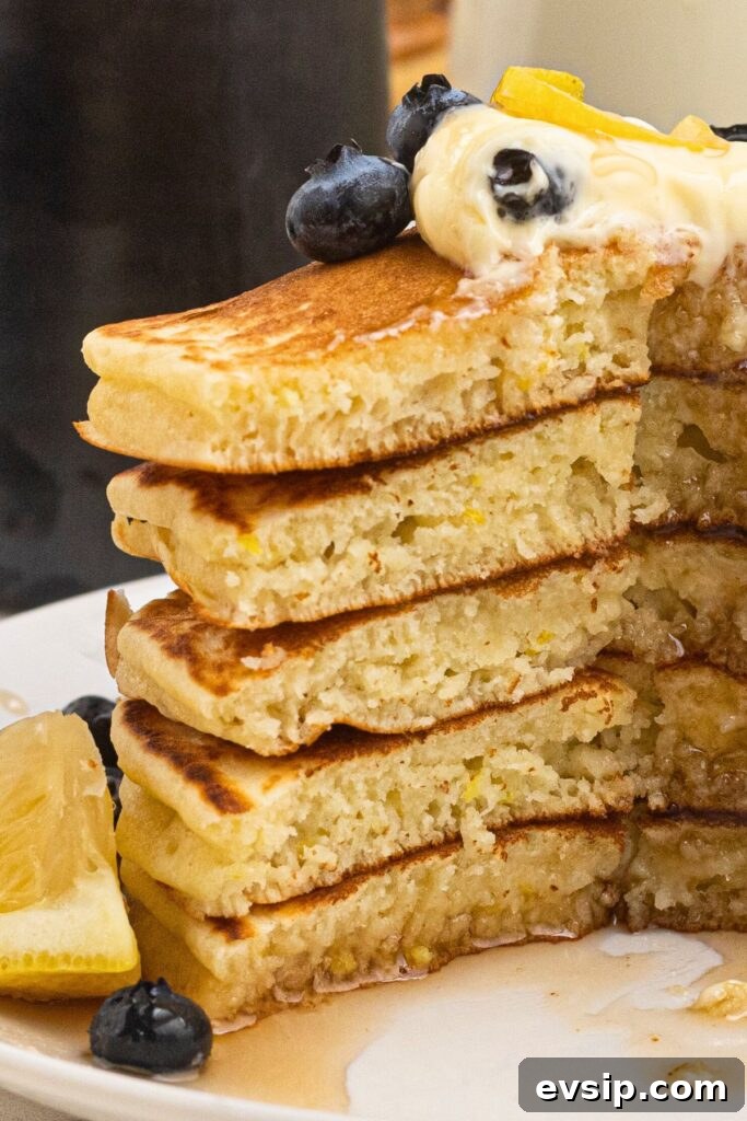 Fluffy Lemon Pancakes with Zesty Syrup Recipe 7 Light and fluffy pancakes stacked on a white plate, drizzled in syrup with butter and blueberries on top.