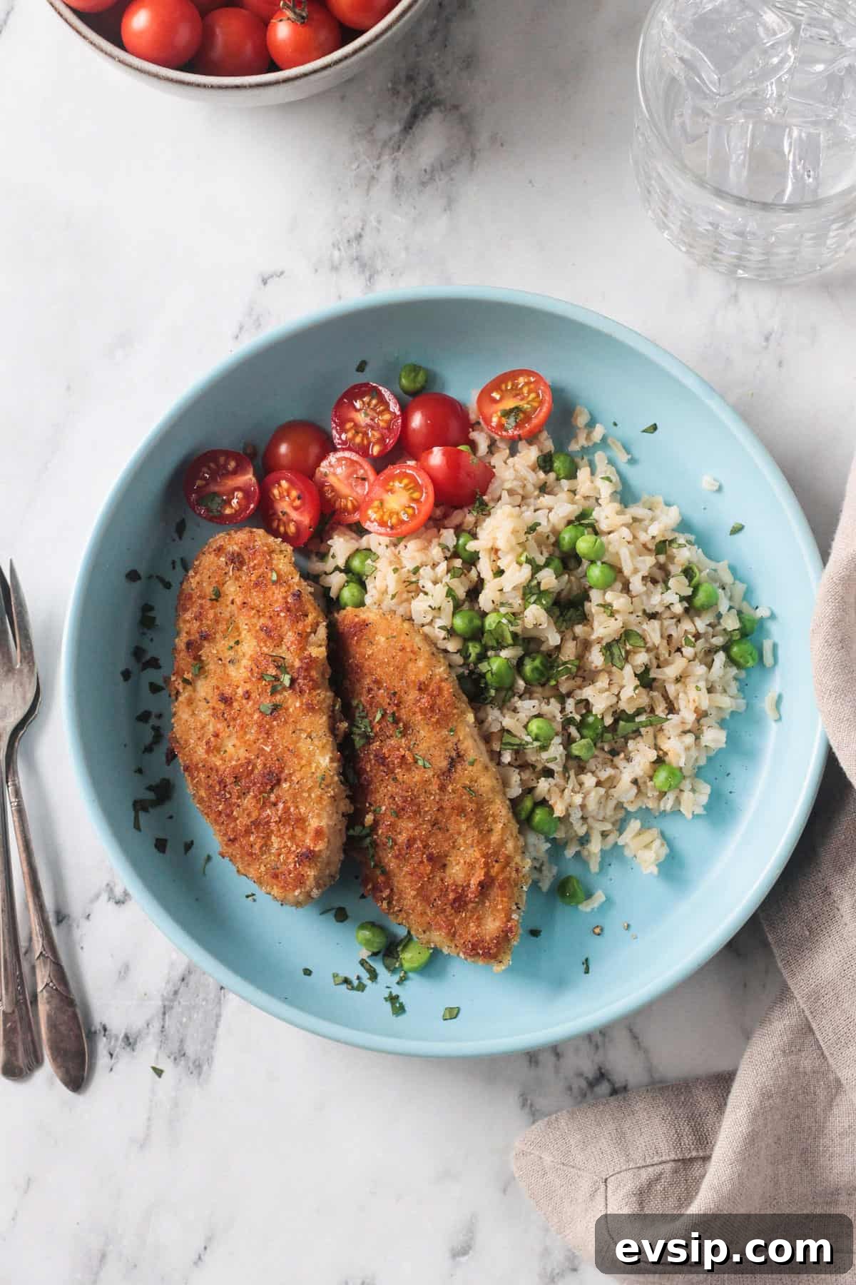 Two breaded vegan chicken cutlets on a blue plate with rice, peas, and tomatoes.