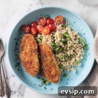 Two breaded vegan chicken cutlets on a blue plate with rice, peas, and tomatoes.