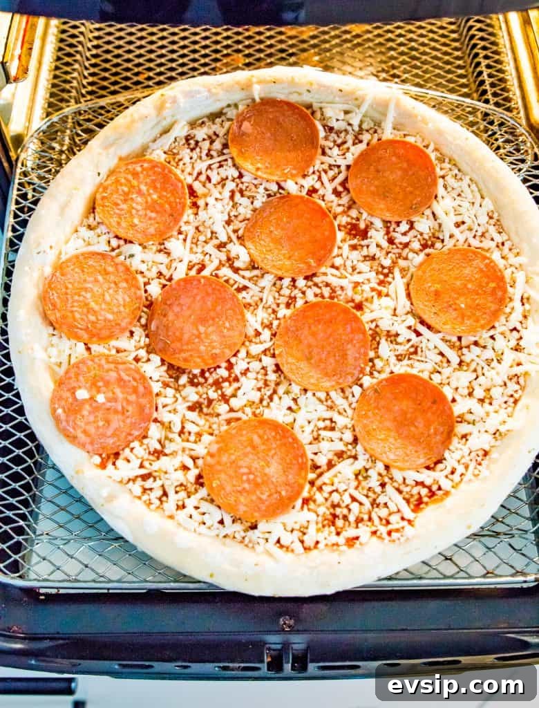 A frozen pizza on an air fryer tray.