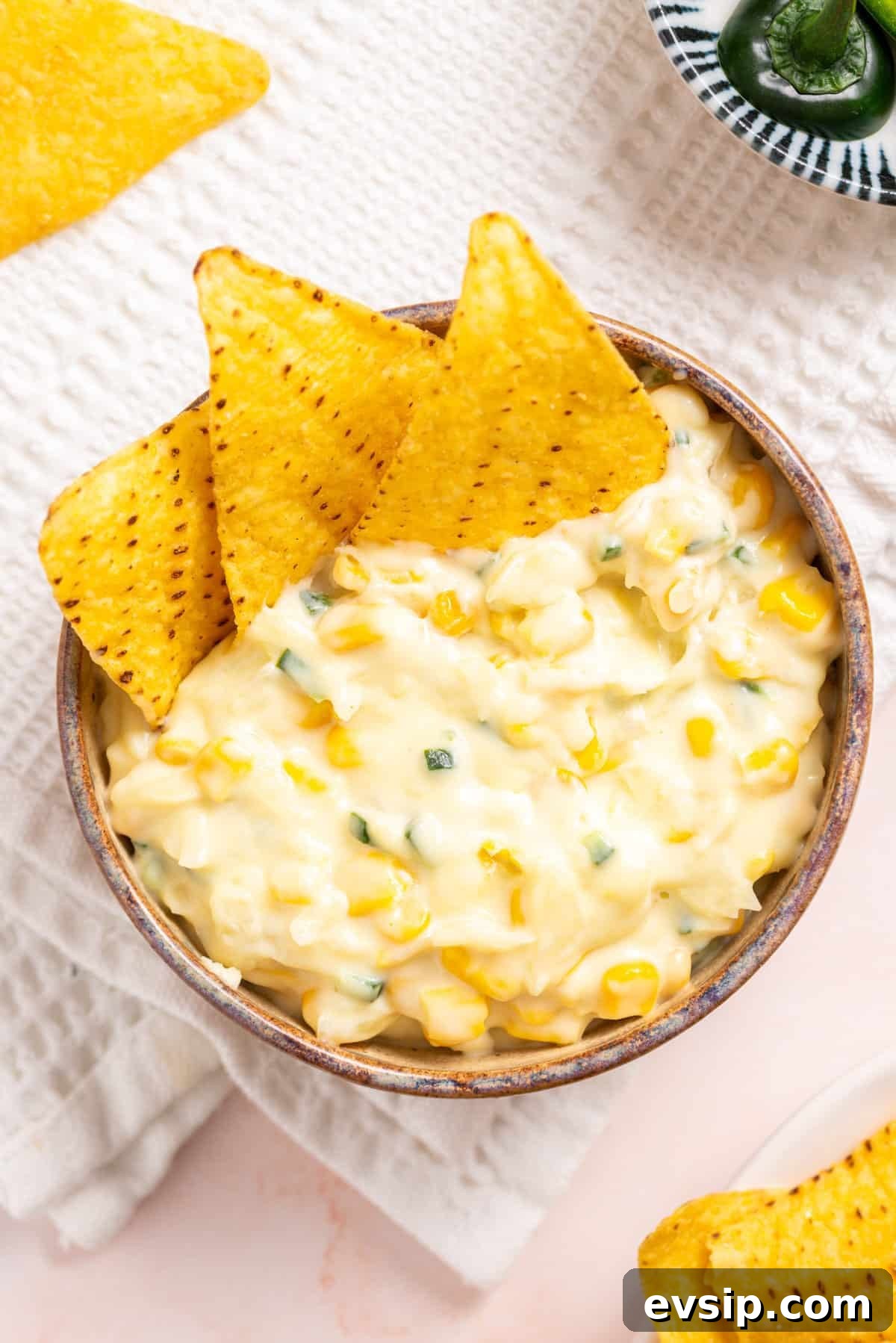 An overhead image of jalapeno corn in a wooden bowl with tortilla chips on the side.