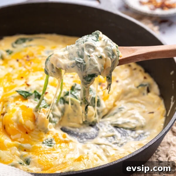 An image of creamed spinach in a cast iron skillet. A wooden spoon with a scoop of creamed spinach hovering over it.