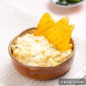An image of jalapeno corn in a wooden bowl with tortilla chips on the side.