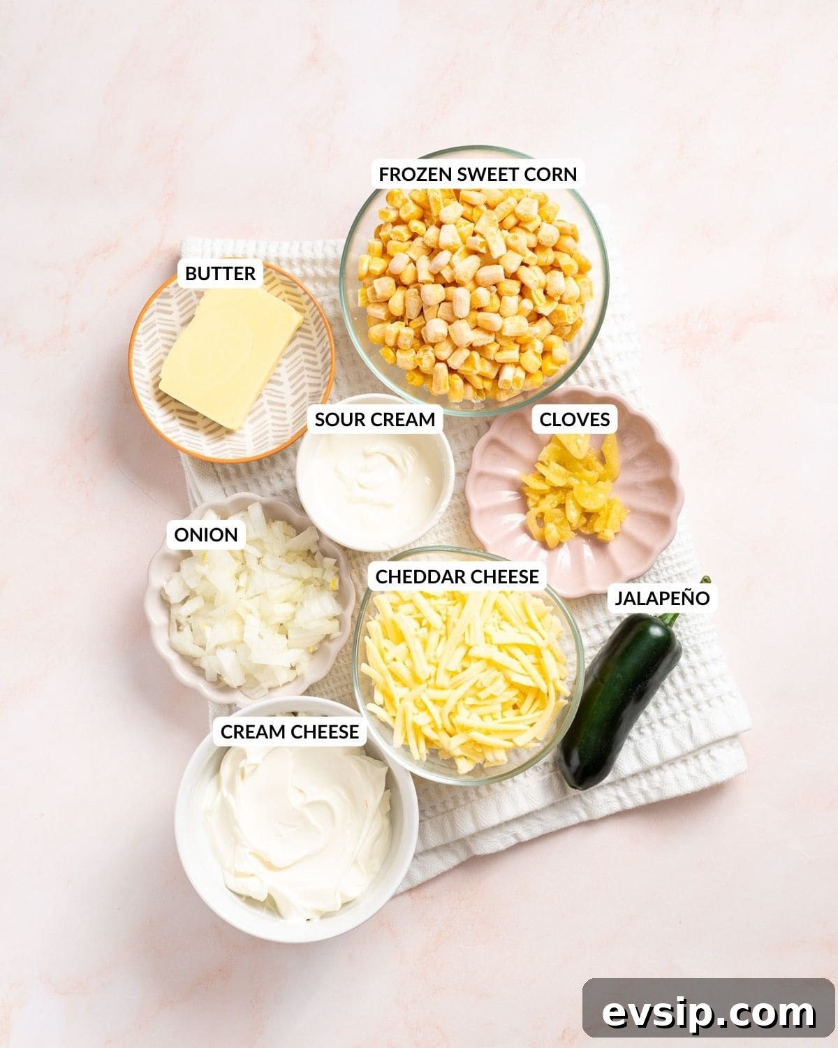 An image of the ingredients of jalapeno corn: sweet corn, jalapenos, sour cream, cream cheese, cheddar cheese, butter, garlic cloves, and onions in separate containers with labels.