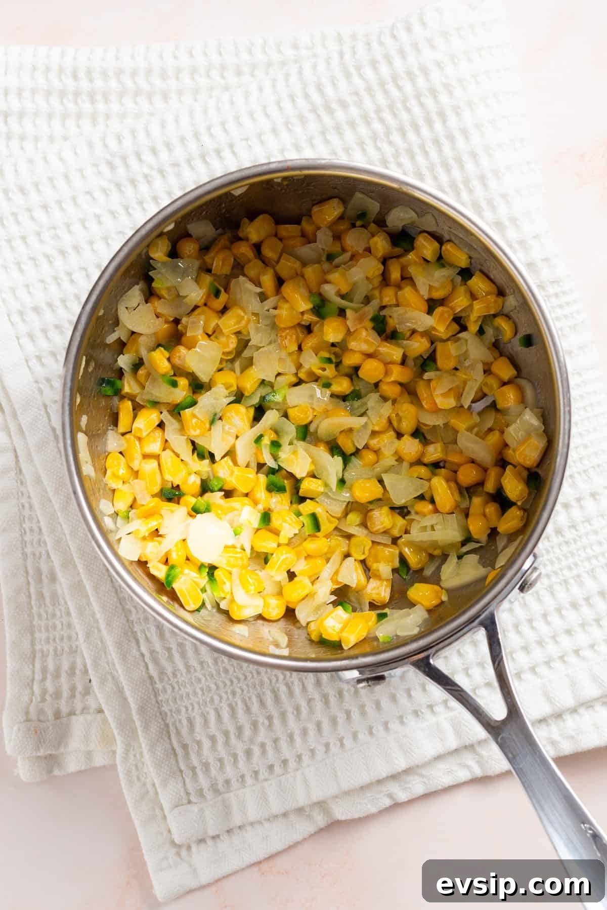 An overhead image of corn kernels added to the saucepan.