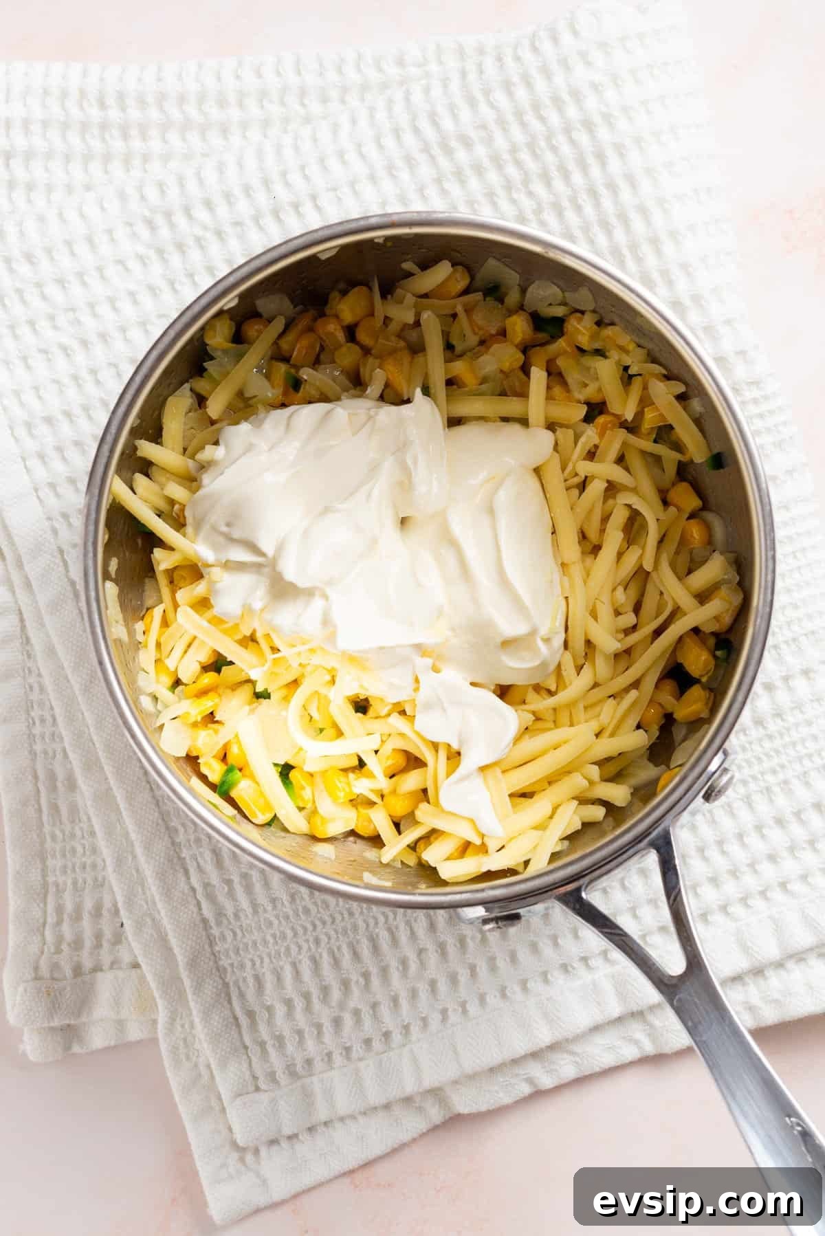 An overhead image of cream cheese, sour cream, cheddar cheese added to the saucepan to melt.