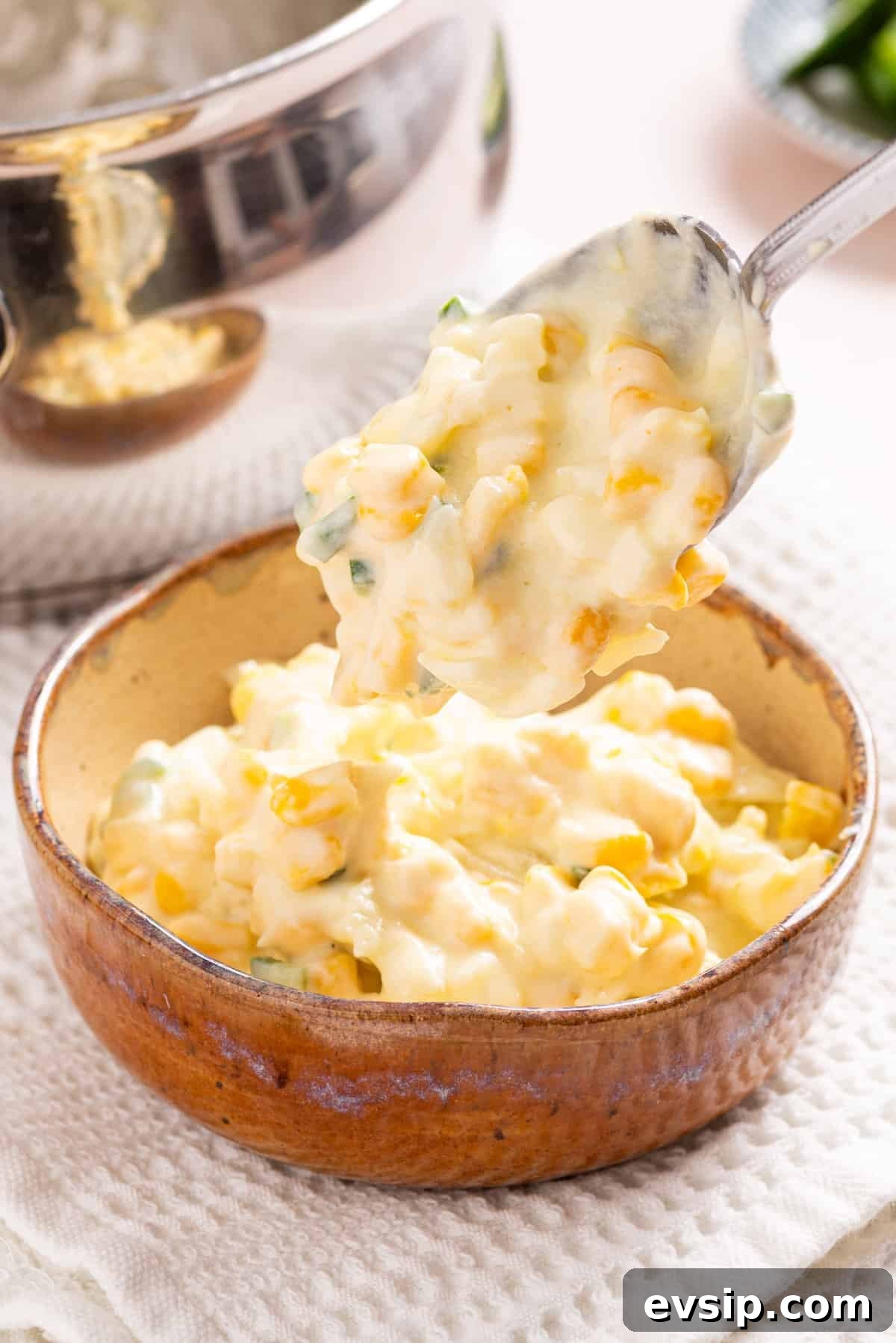 An image of jalapeno corn in a wooden bowl with a spoon scooping a spoonful of jalapeno corn.