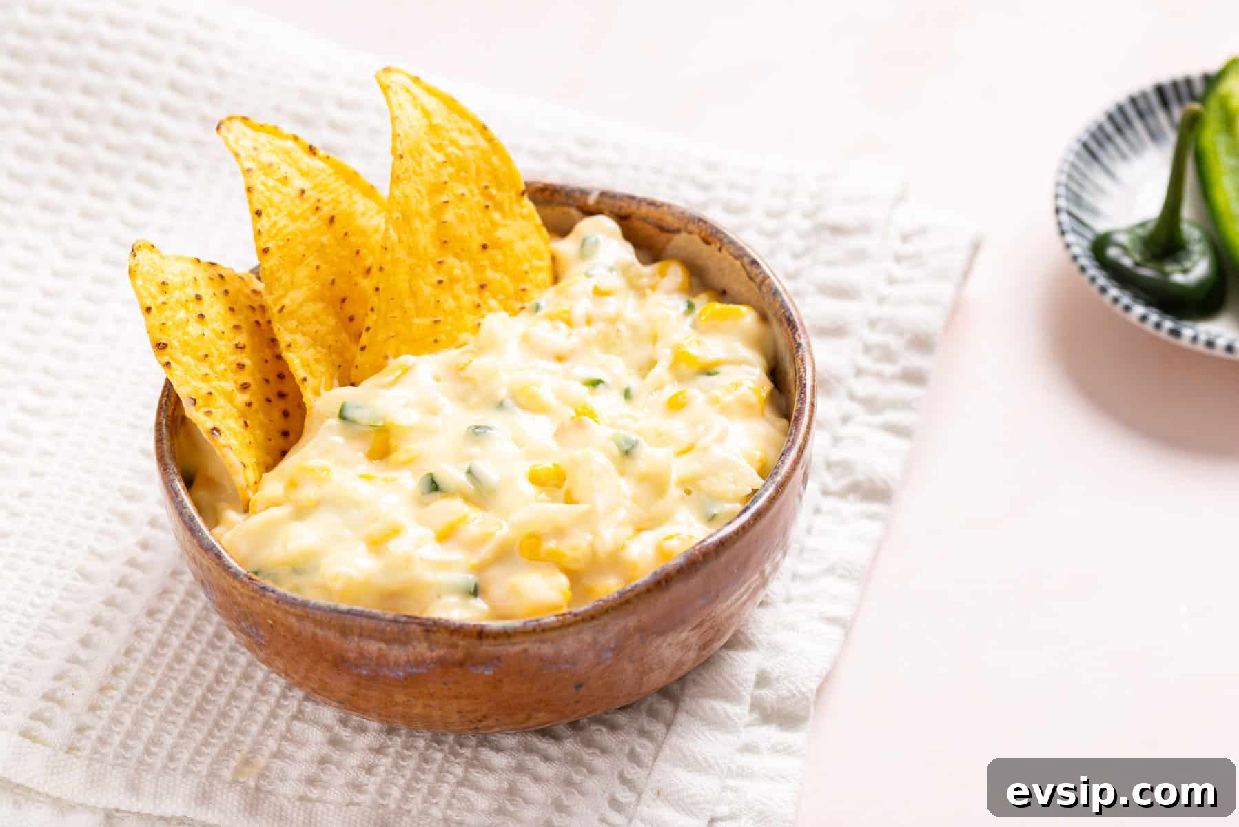 An image of jalapeno corn in a wooden bowl with tortilla chips on the side.