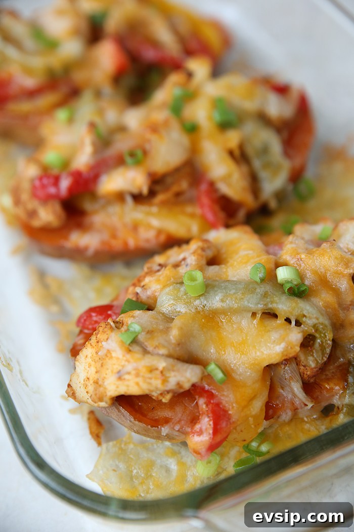 A glass 9x13 baking dish with three sweet potatoes cover in chicken fajitas with cheese melted on top and sliced green onions on top of the cheese and with cheese melted on the dish.