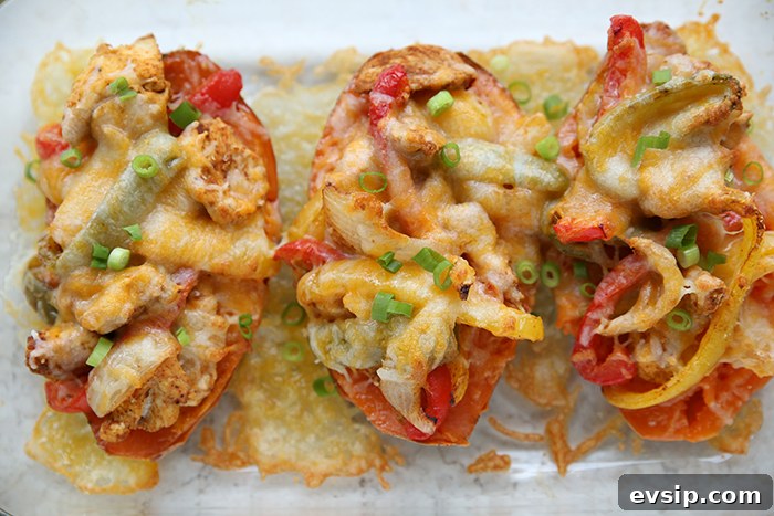 Three baked sweet potato halves stuffed with chicken fajita mixture topped with melted cheese and sliced green onions in a glass 9x13 baking dish with cheese melted around the bottoms of the potatoes.