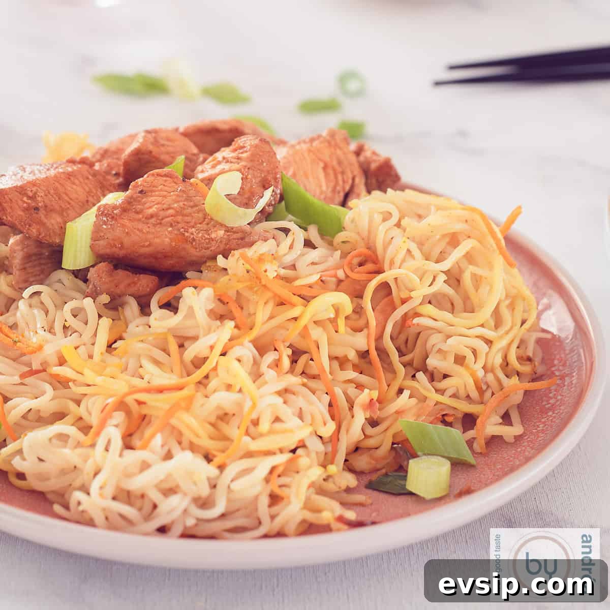 A square photo with a pink plate with noodles and cantonese chicken. A white background.