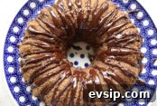 A whole chocolate zucchini spice bundt cake with chocolate ganache drizzled down the sides and in the middle sitting on a round Polish pottery plate with white polka dots and a dark blue background.