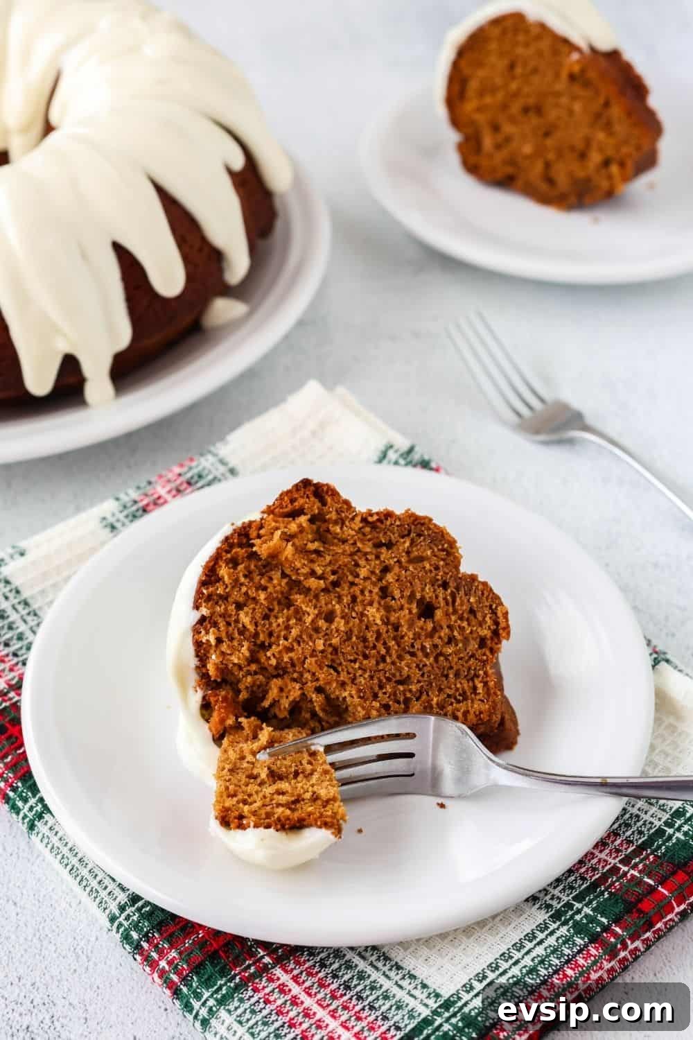 slice of gingerbread bundt cake on a white plate, with the remaining cake and another slice in the background.