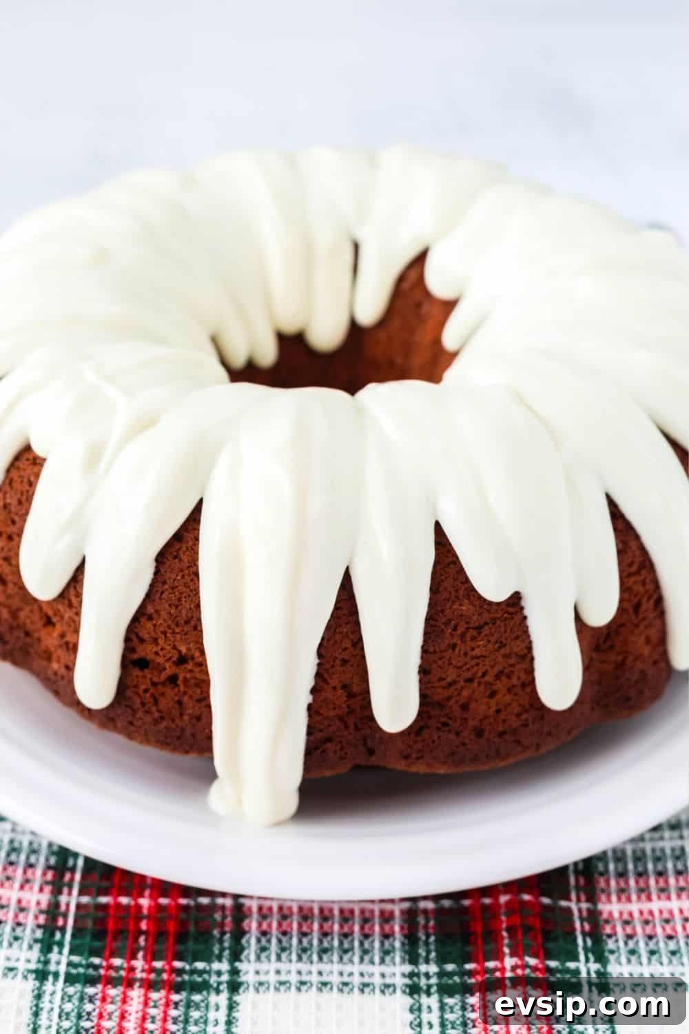 side view of a cake mix gingerbread cake, topped with cream cheese frosting. It's on a white plate, resting on a Christmas tea towel.