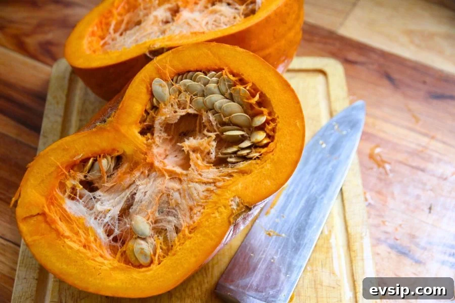 A fresh pumpkin cut in half on a cutting board, ready to have seeds removed.
