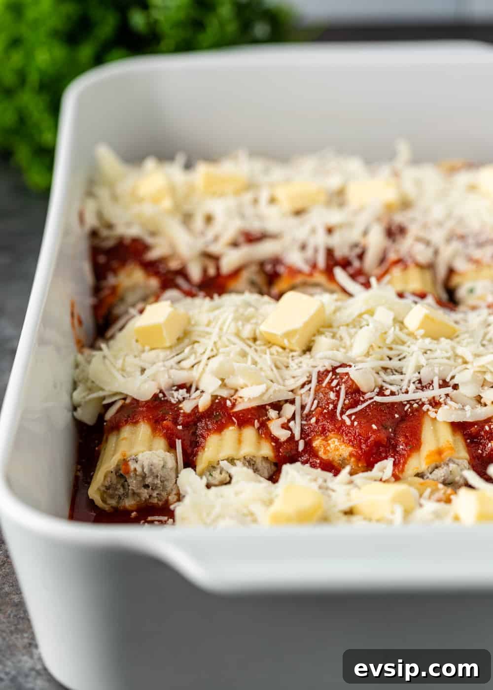 Cheesy Beef Manicotti Recipe with Homemade Marinara 6 authentic italian manicotti in a baking dish with sauce, cheese, and butter on top before baking