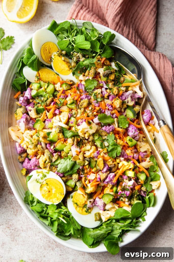 Orange and purple cauliflower salad with spring greens and a hard boiled egg. Serving utensils and a pink cloth on the table.