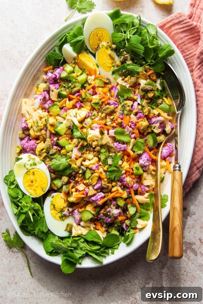 Cauliflower salad in large white platter with serving utensils.