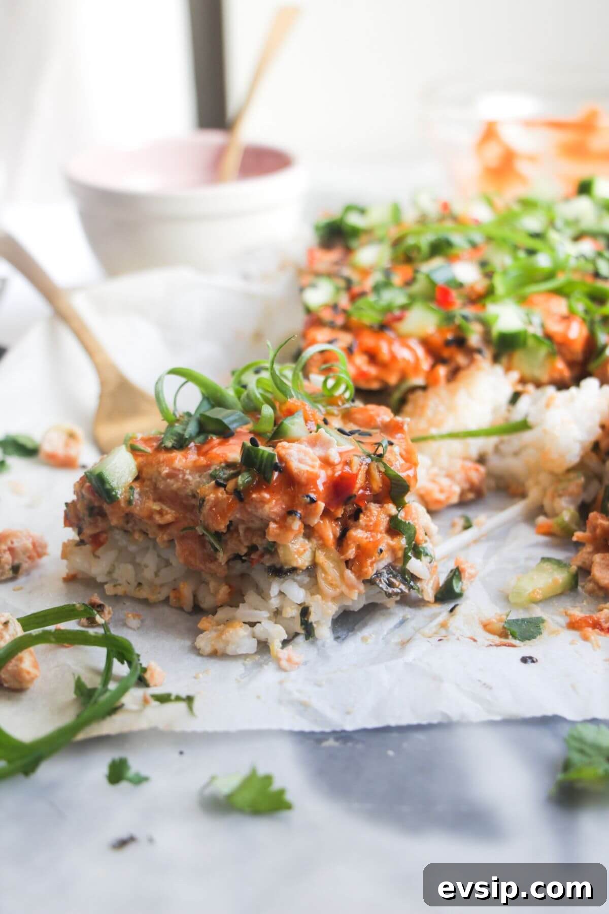 Close up of a piece of salmon sushi bake, with the rest of the bake in the background.