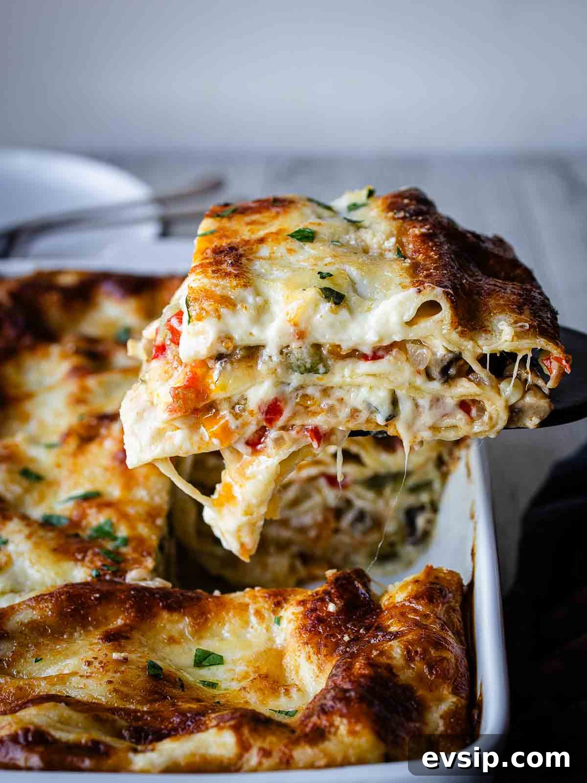 A slice of vegetable lasagna with white sauce being lifted out of a baking dish.