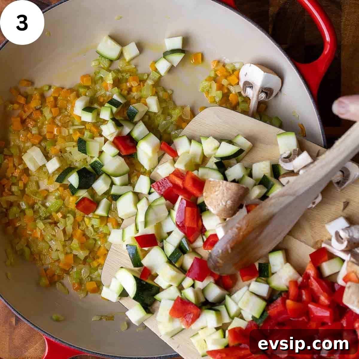 Adding chopped mix of vegetables to a pan of cooked chopped onion, carrot and celery.
