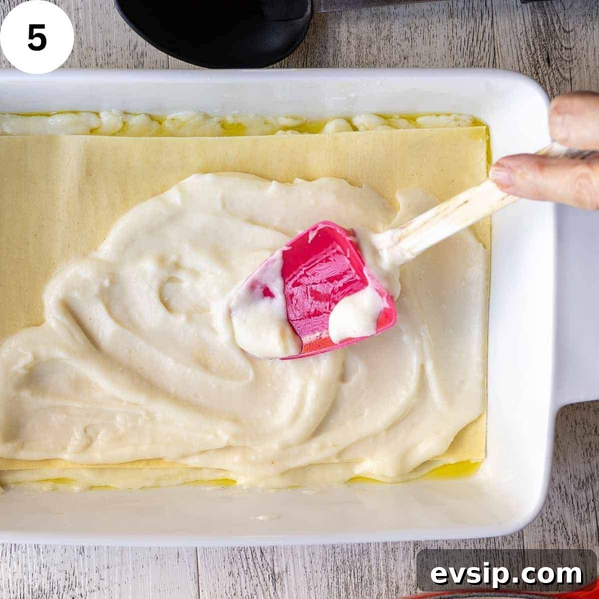 Spreading white sauce on lasagna noodle in a lasagna pan.
