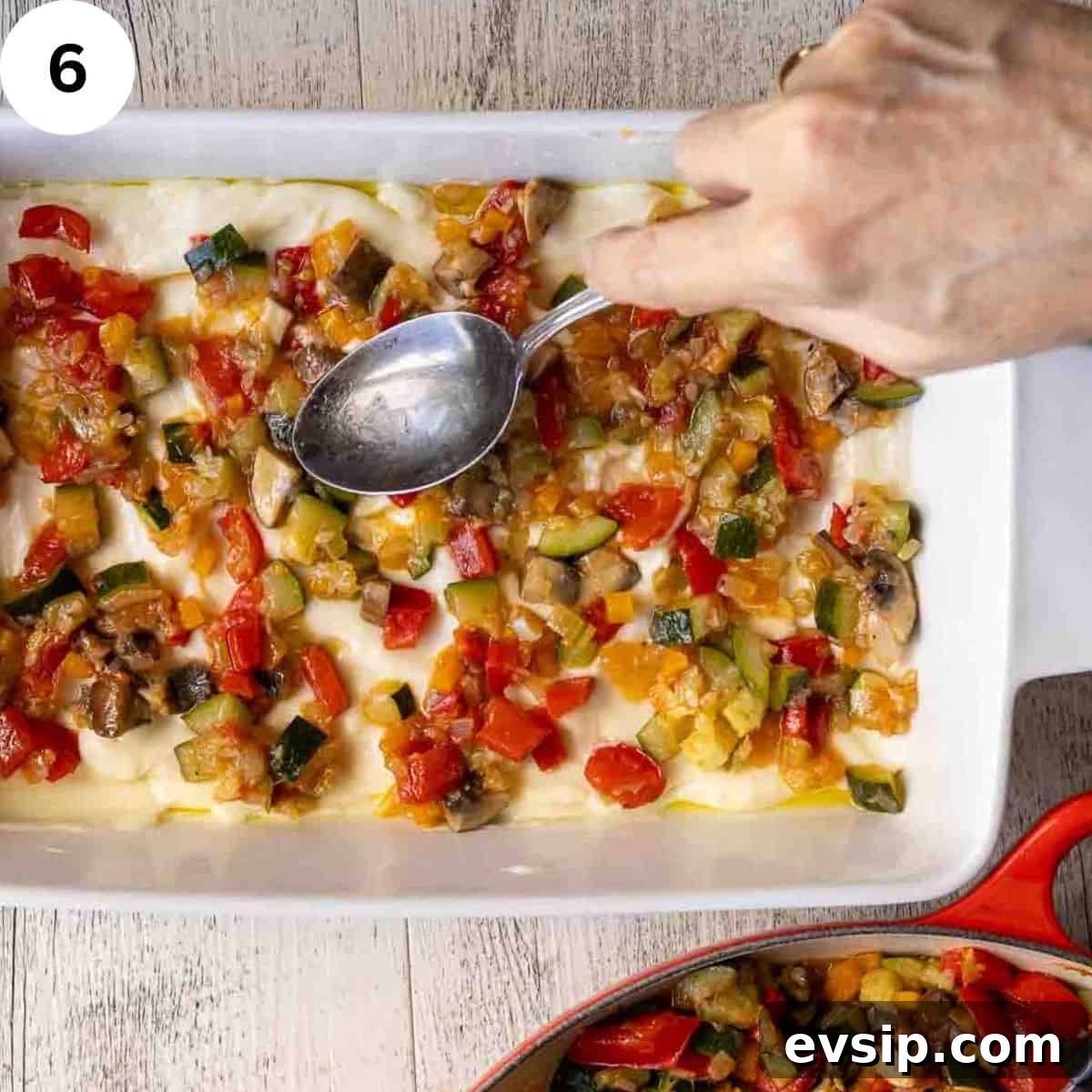 Spreading a mixture of cooked vegetables over white sauce and lasagna noodles in a lasagna pan.