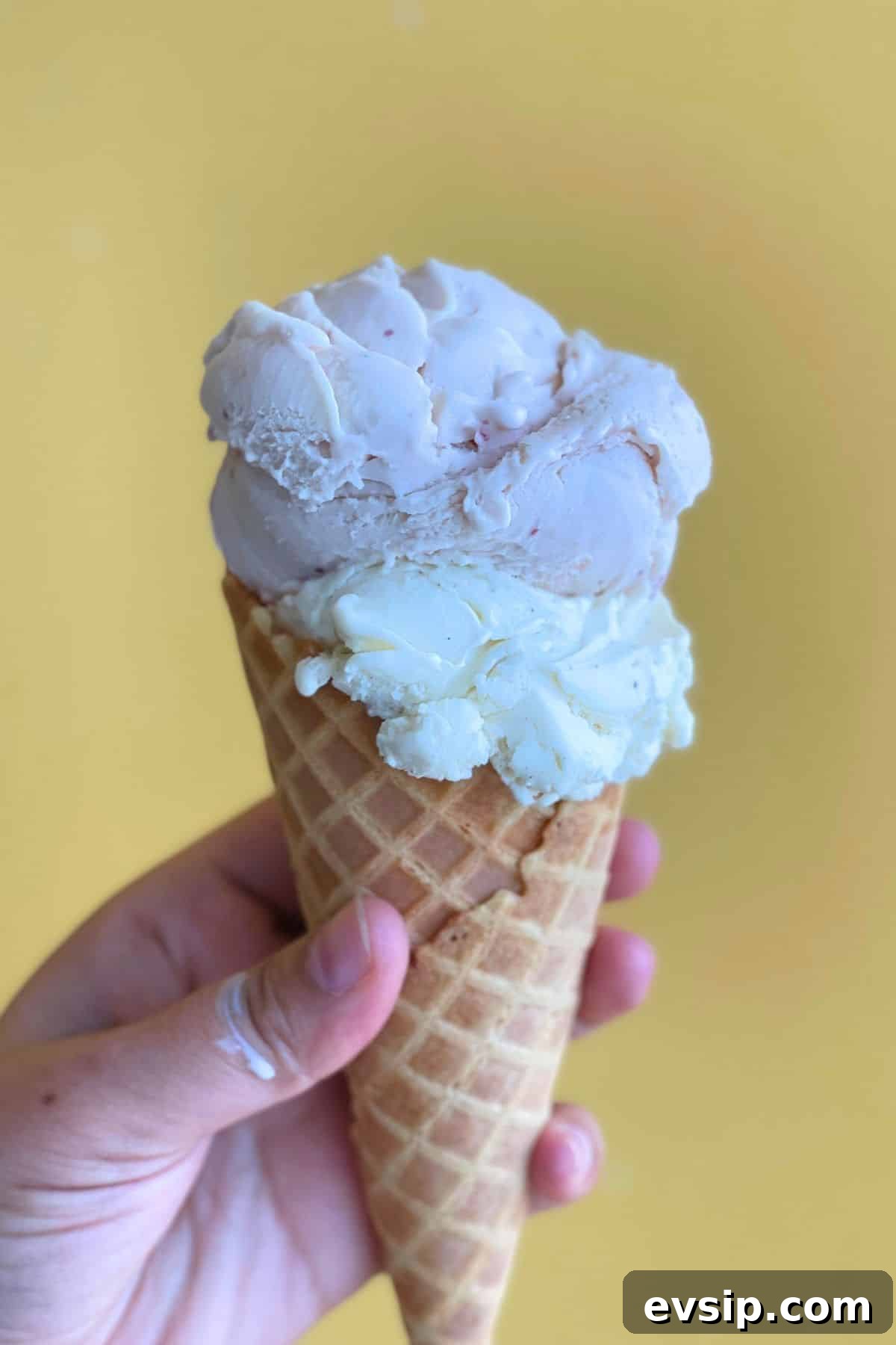 A hand holding ice cream cone with homemade ice cream.