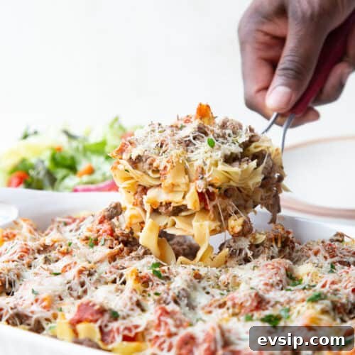 hand lifting a scoop of pizza casserole from a white casserole dish.