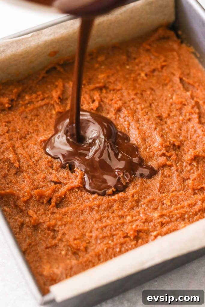 Pouring melted chocolate over pumpkin mixture in a baking pan