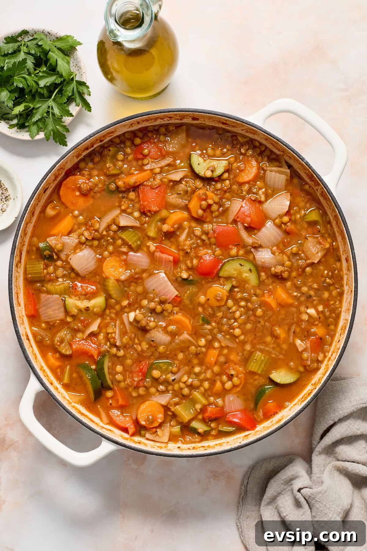Large pot of Lentil Stew, with a cloth, some parsley and olive oil on the side of pot.