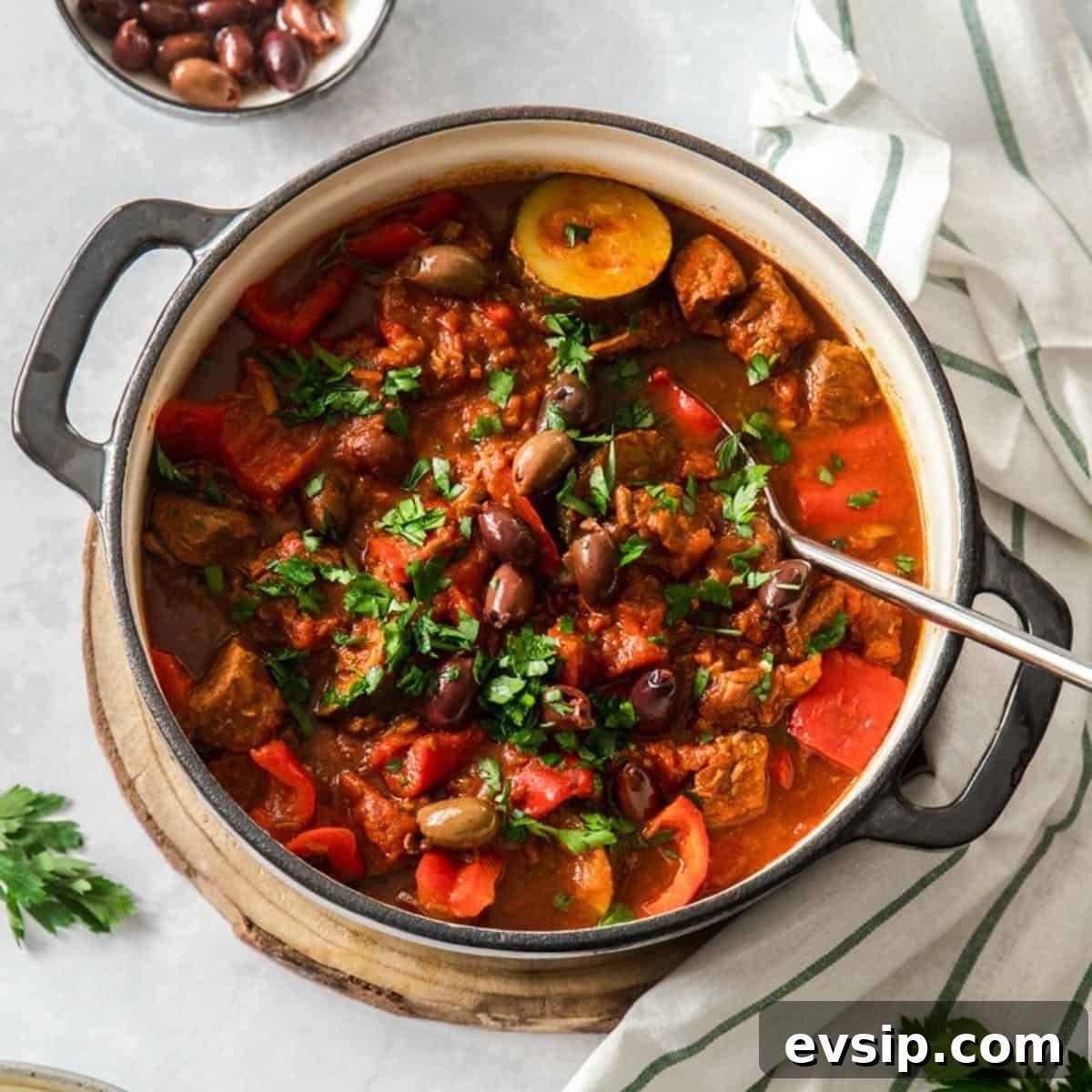 Dutch oven beef stew, with a silver serving spoon in dish which is garnished with parsley.