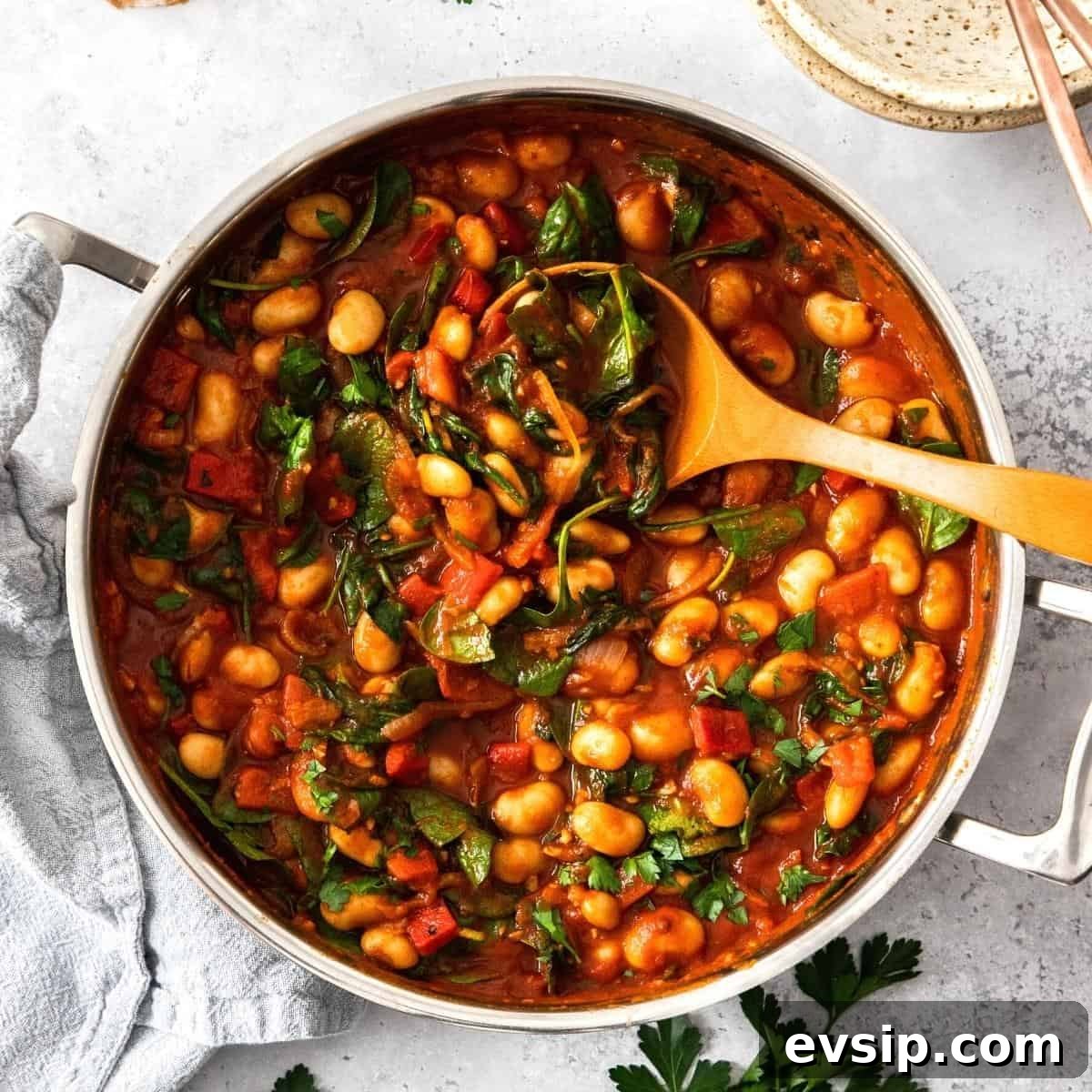 Round saucepan of butter bean stew, with a wooden spoon sitting in the pot.