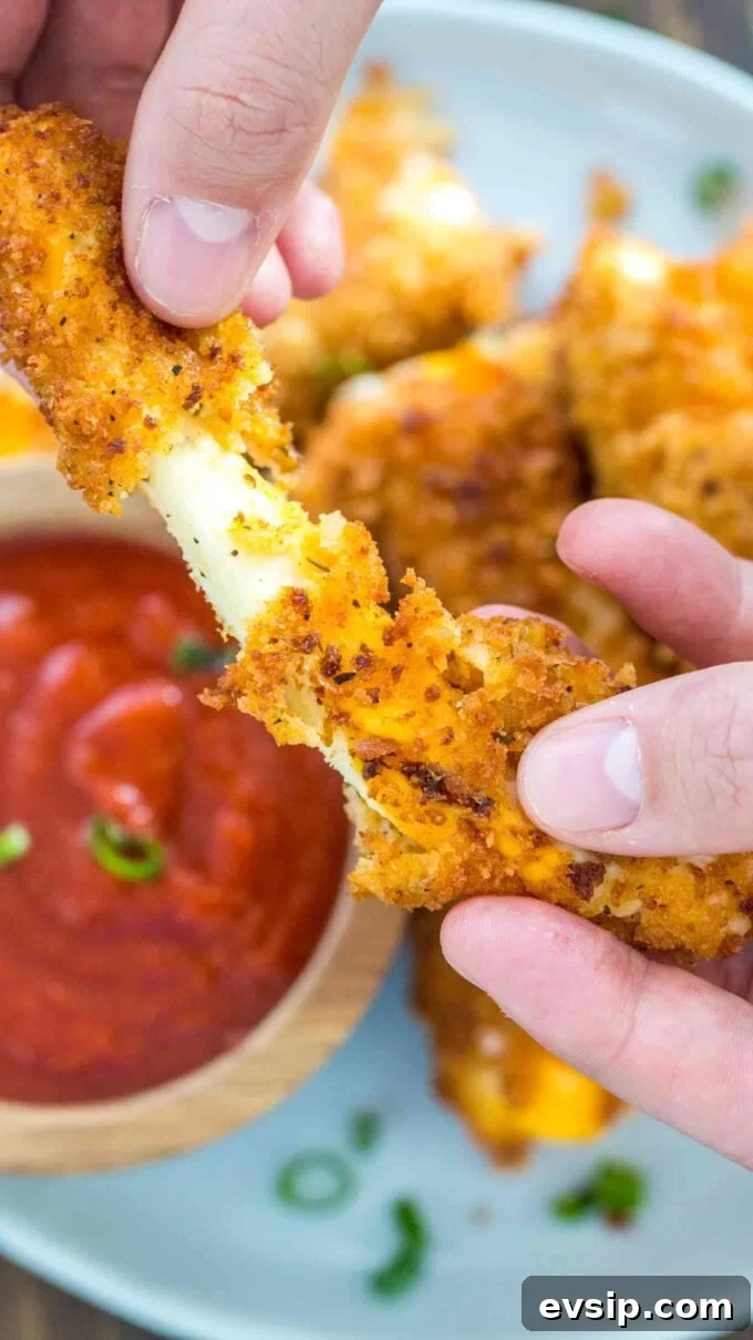 Pulling a fried cheese stick with marinara sauce on the side.