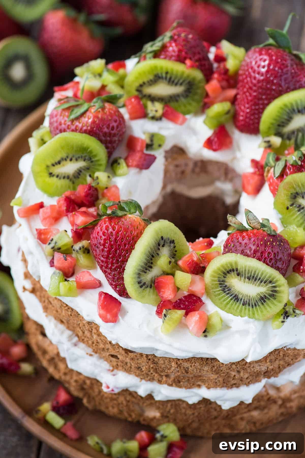 Light and Fluffy Strawberry Angel Food Cake Recipe 7 strawberry angel food cake topped with whipped cream, whole strawberries, chopped strawberries and kiwi on wooden serving tray
