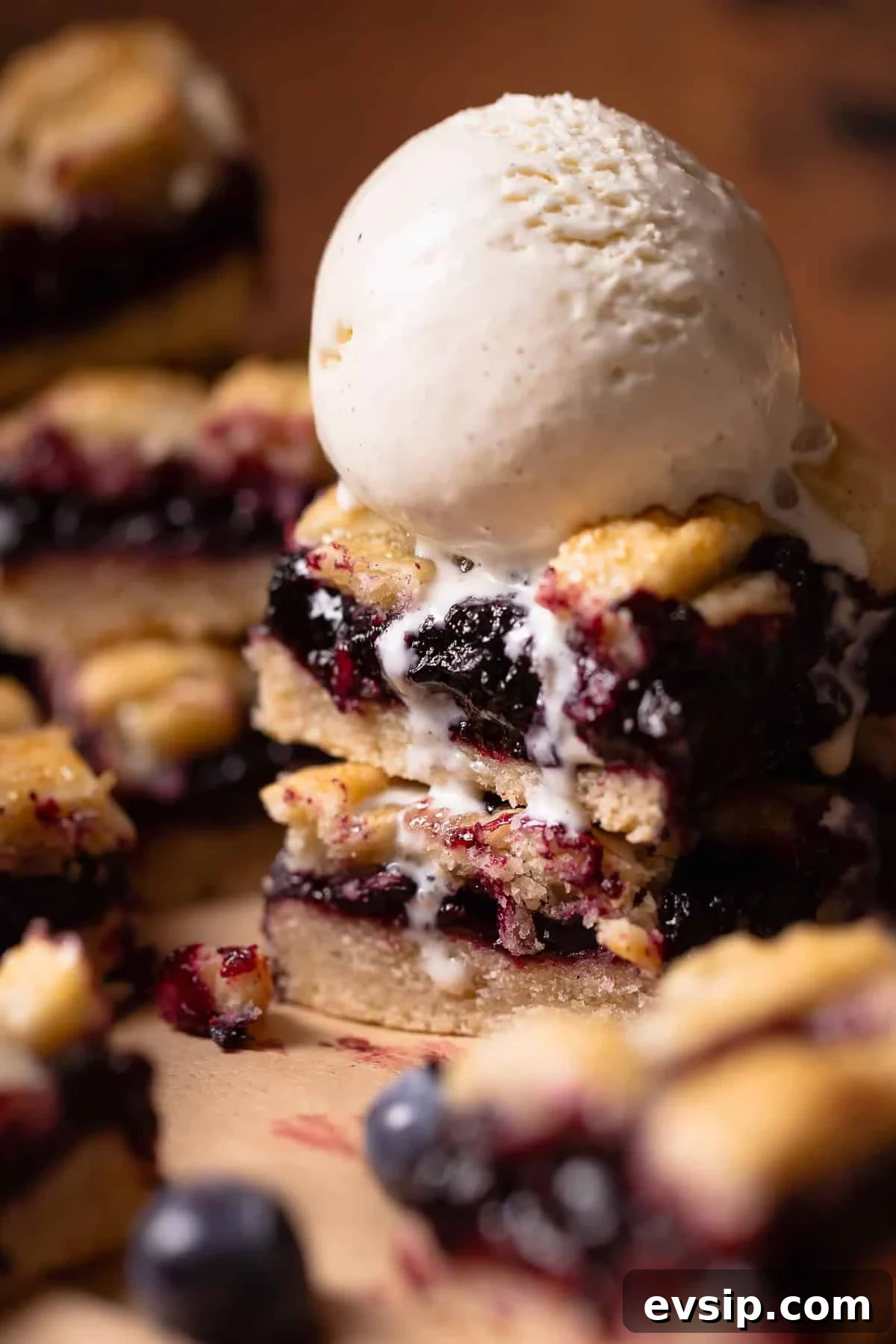 Two blueberry pie bars topped with a scoop of vanilla ice cream.